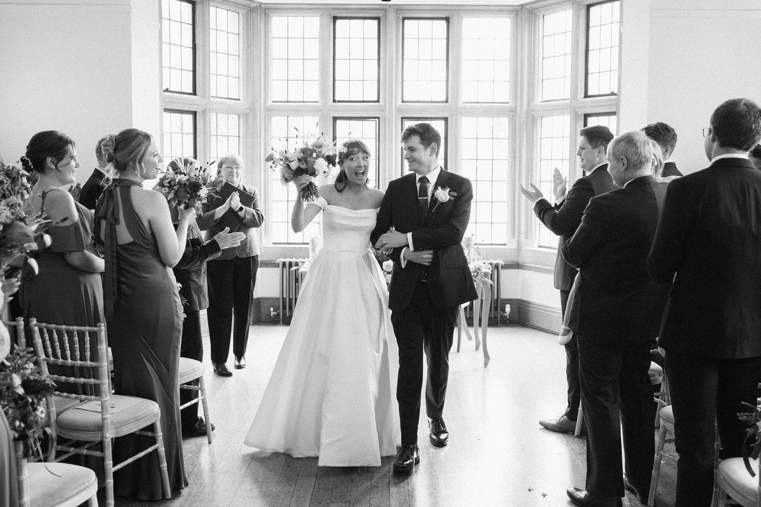 Black and white photo of a joyful bride and groom walking down the aisle after their wedding ceremony.