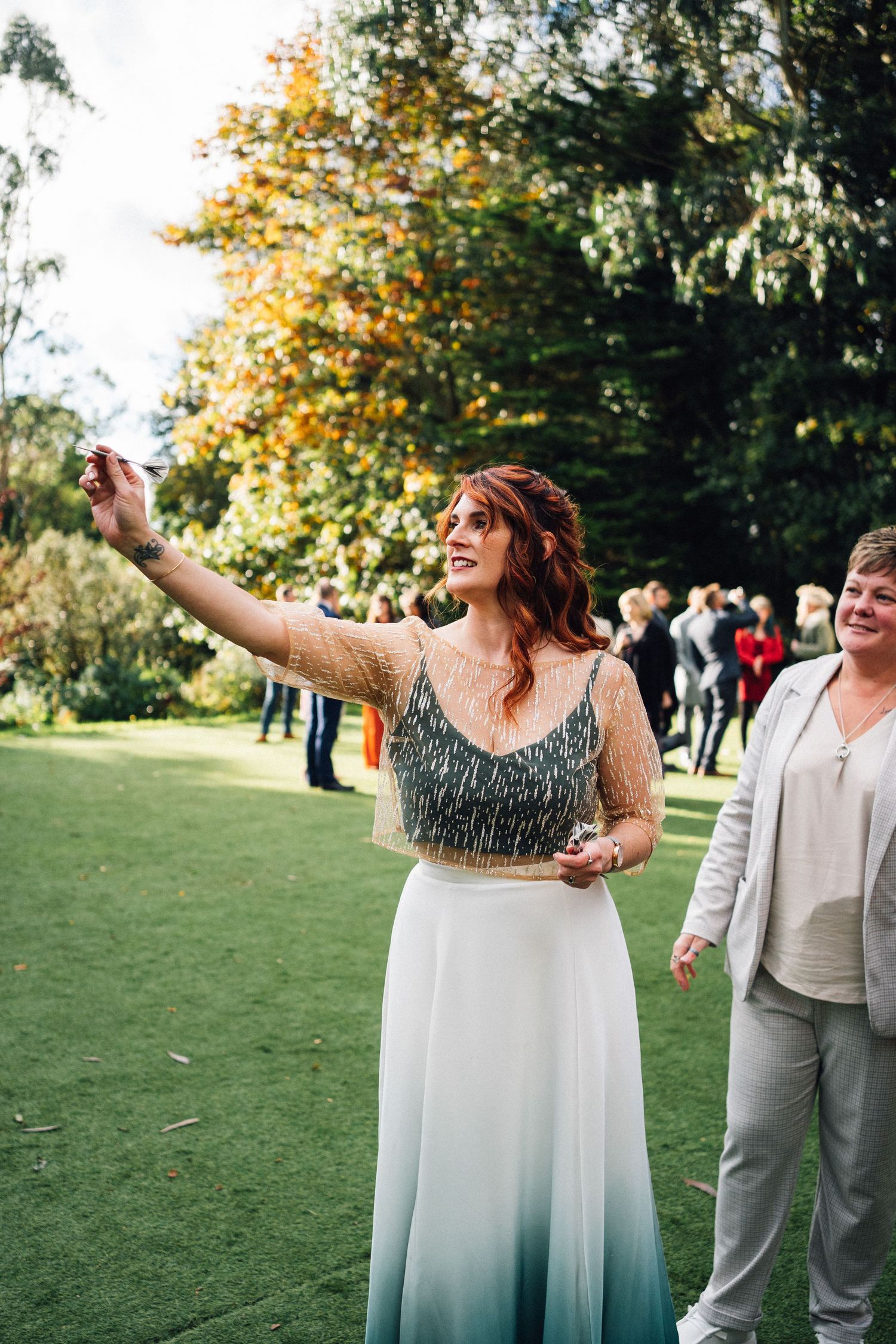 Two people dancing joyfully on a grassy lawn during a sunny outdoor celebration with autumn trees in the background.