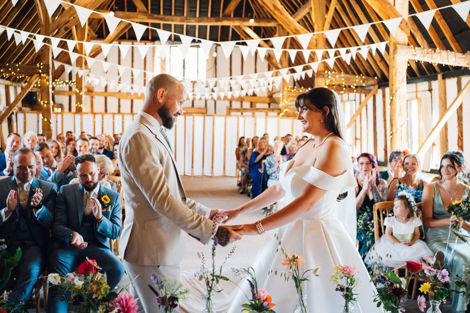Wedding celebration inside a rustic barn venue with exposed wooden beams and string lights creating a warm atmosphere.