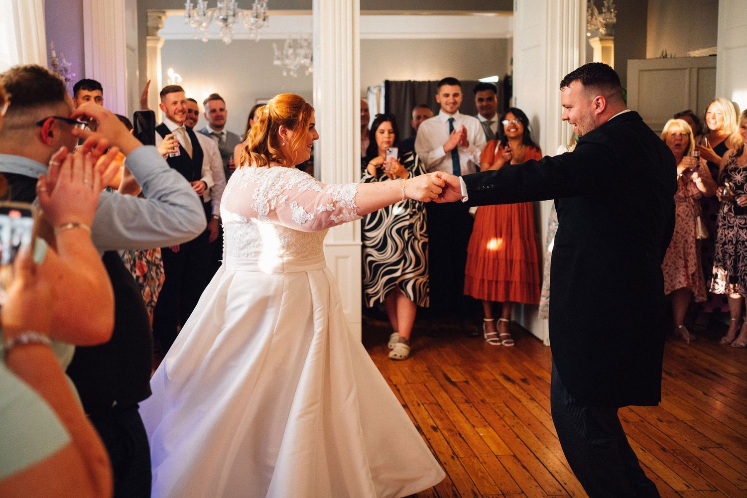 Wedding reception dance floor filled with celebrating guests in an elegant ballroom with wooden floors.