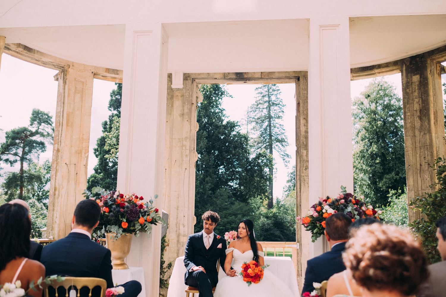 Wedding ceremony setup with white columns and natural light streaming through windows.