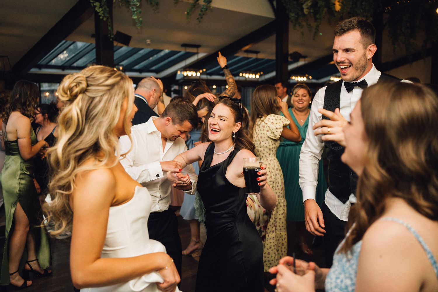 Wedding celebration with guests dancing under string lights and decorative greenery.