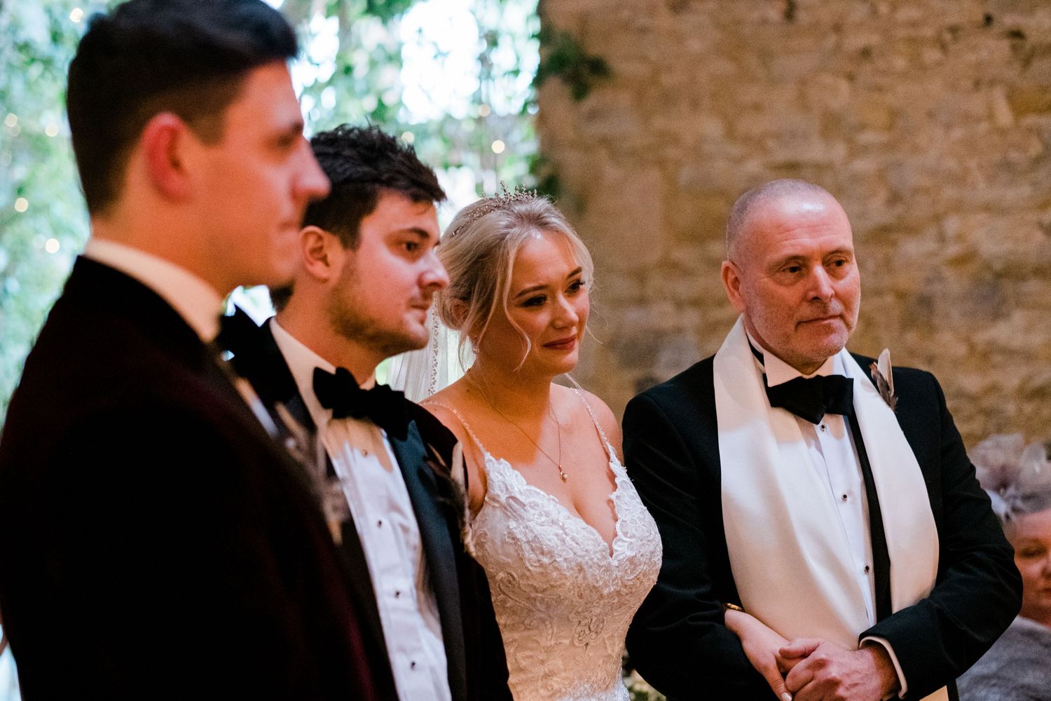 Elegant wedding reception with guests in formal attire against stone wall backdrop.