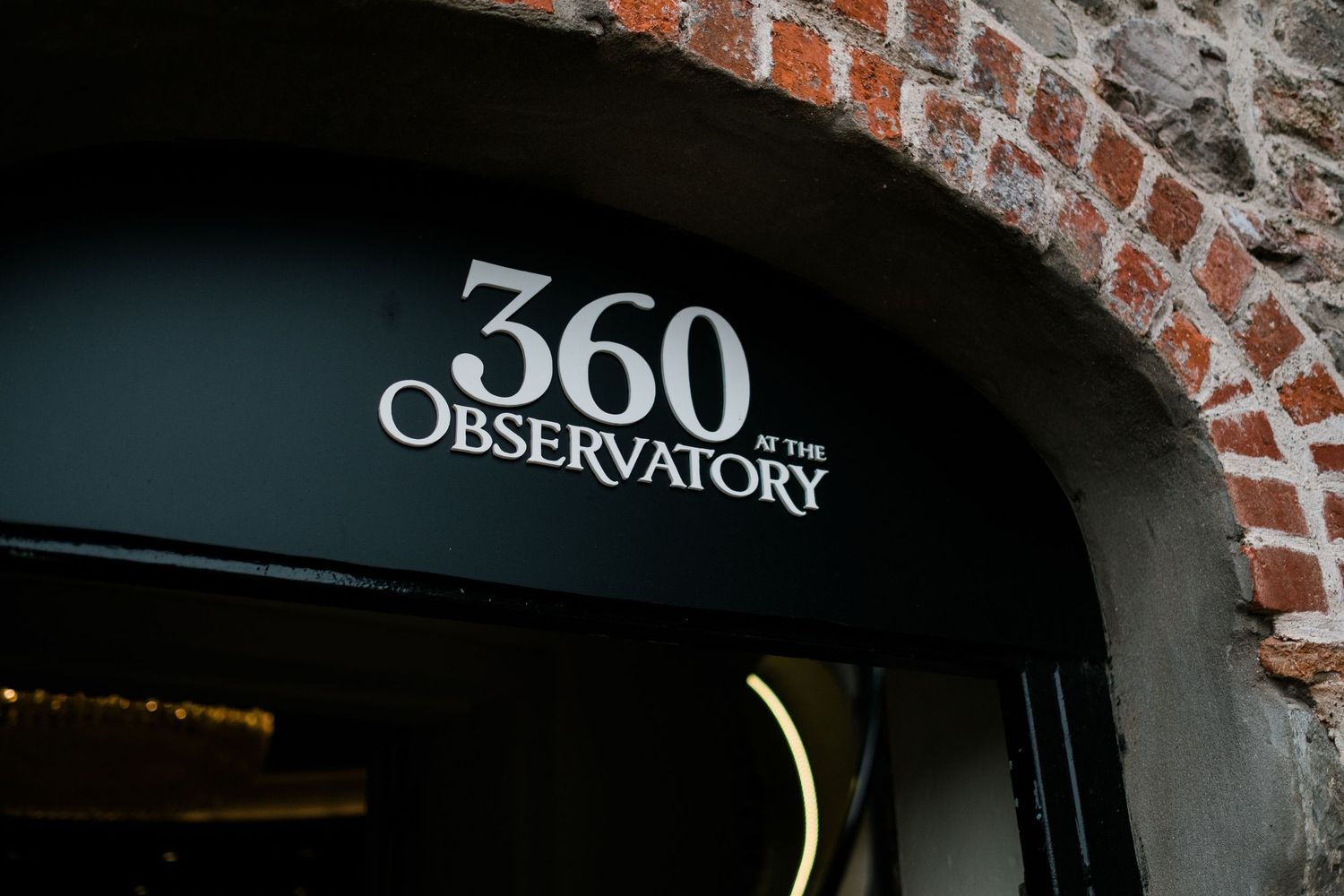 Black awning sign for 360 Observatory restaurant set in a rustic brick archway entrance.