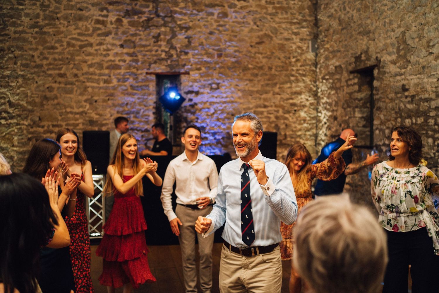 Wedding reception crowd dancing and celebrating in a historic brick venue with ambient lighting.
