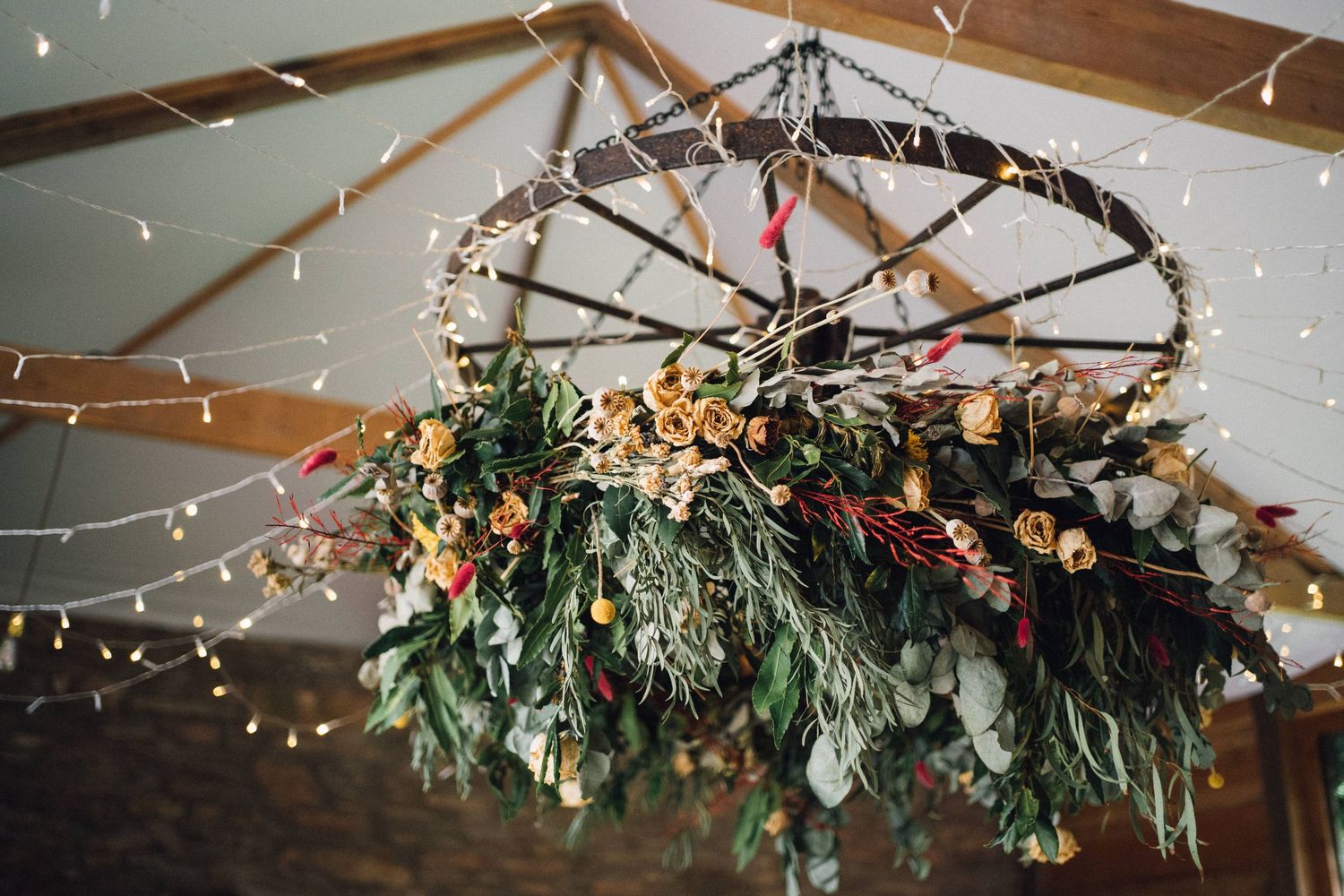 Elegant wedding reception ceiling decorated with greenery, flowers and string lights.