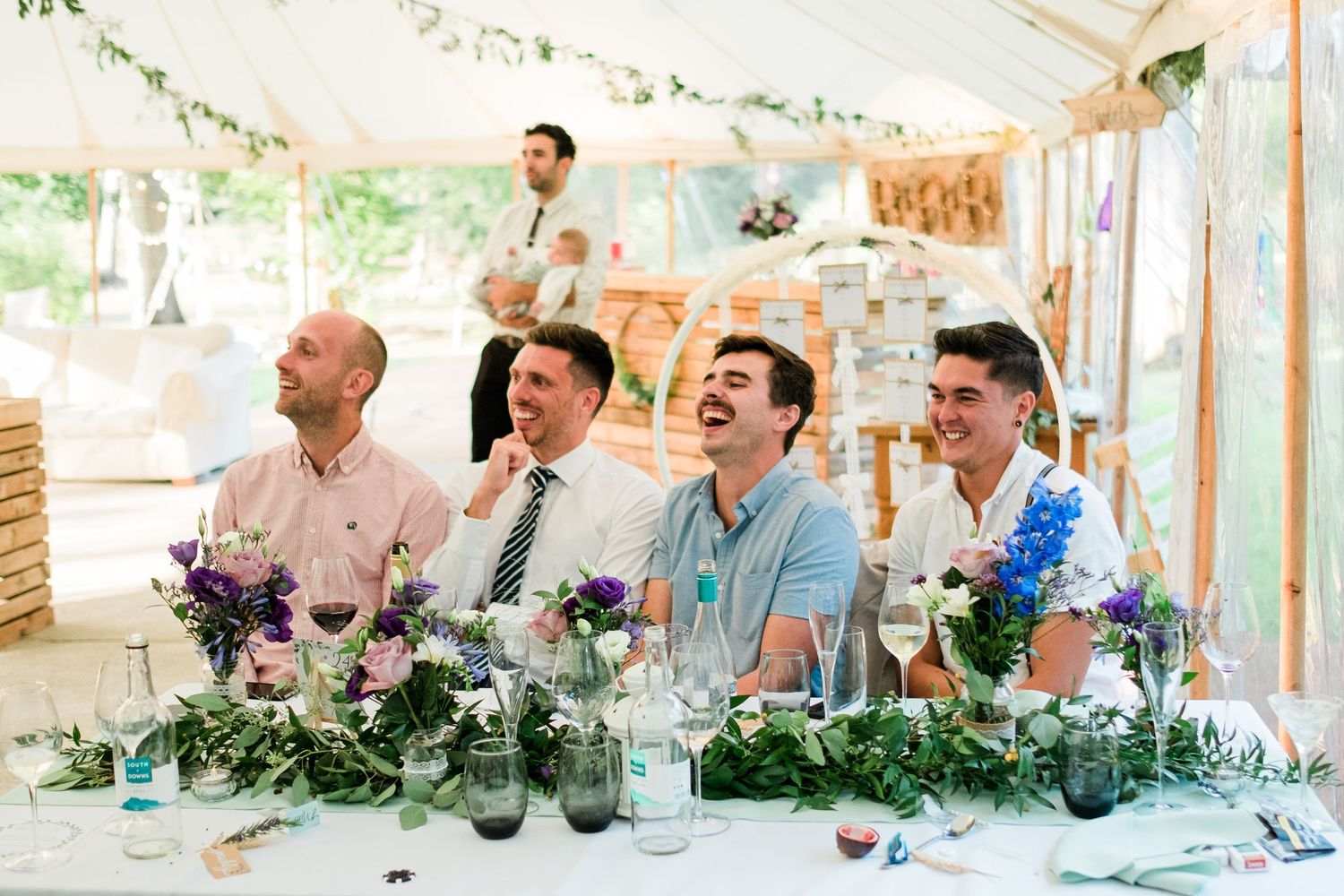 Long banquet tables decorated with floral centerpieces and greenery in an elegant wedding tent.
