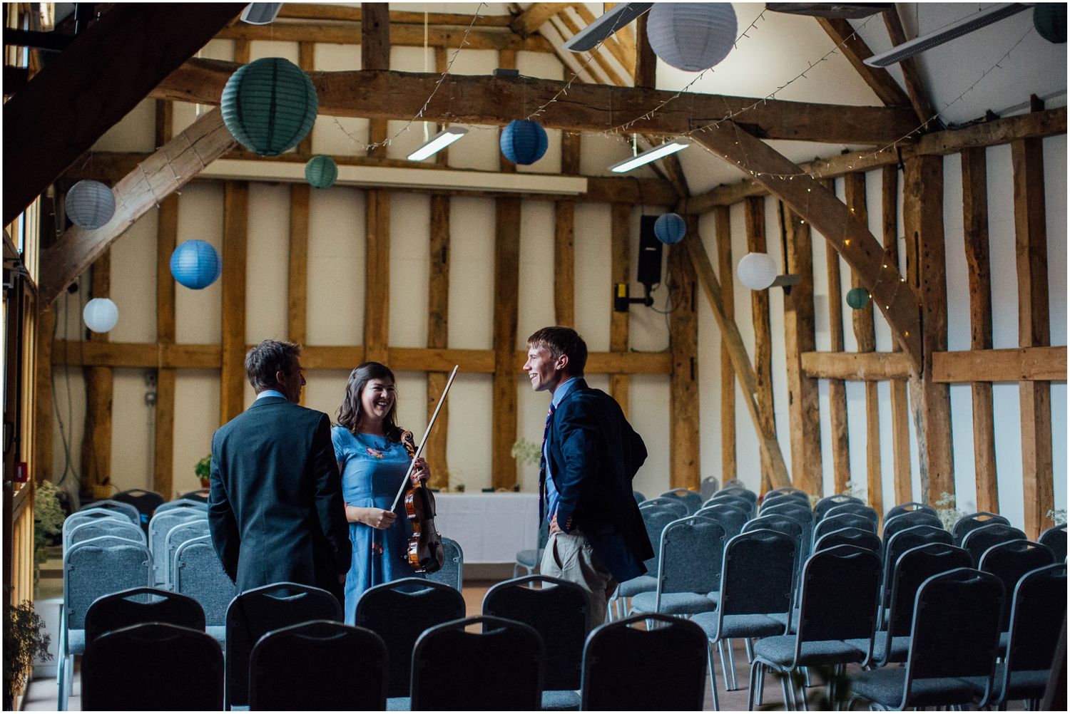Interior of a rustic barn venue with exposed wooden beams and rows of chairs set up for an event.