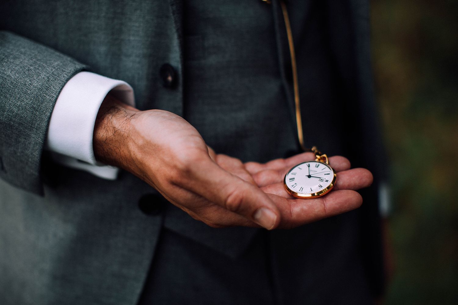 A close-up shot of hands holding an antique pocket watch against a formal suit.
