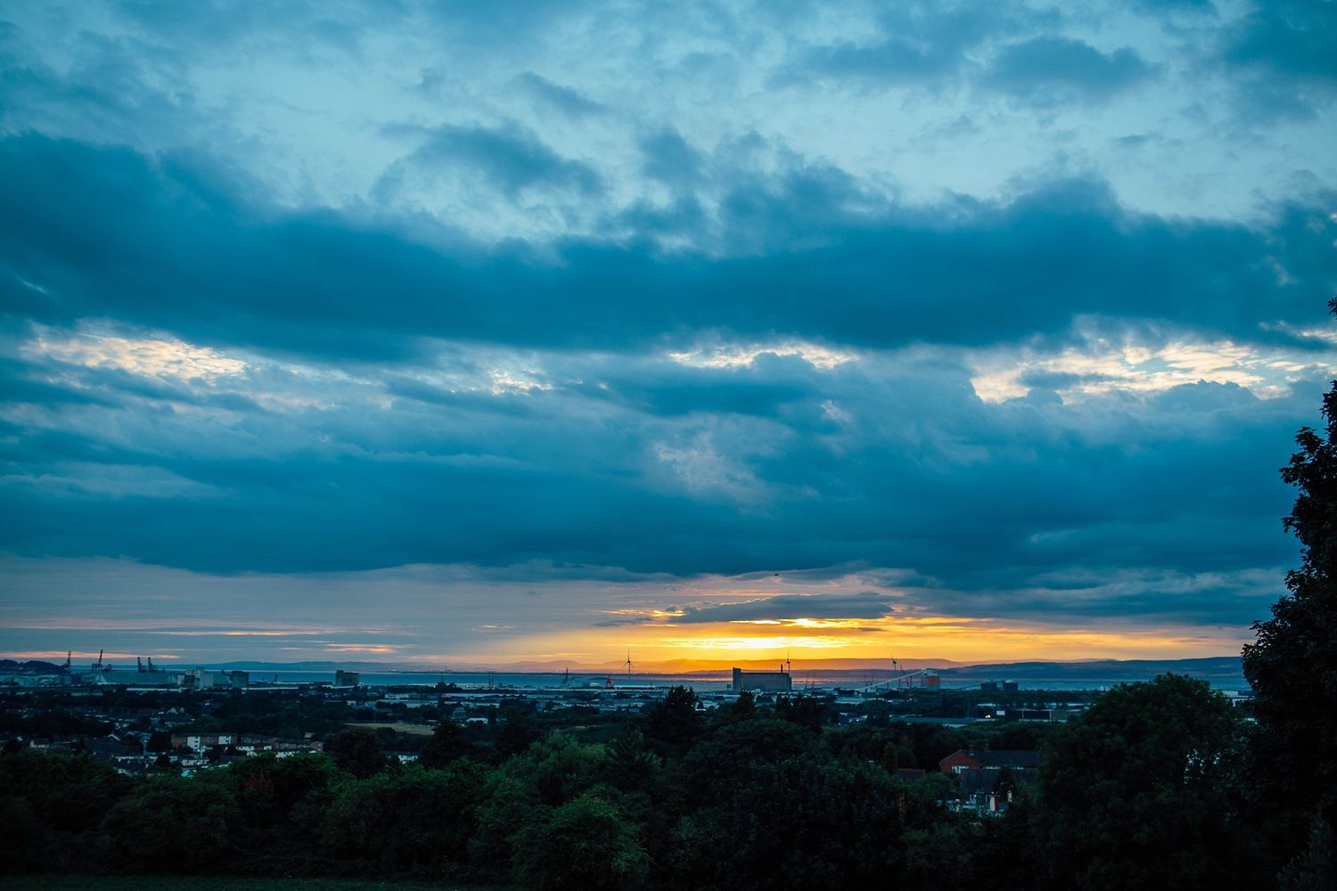 Dramatic panoramic sunset over a cityscape with stormy blue clouds.