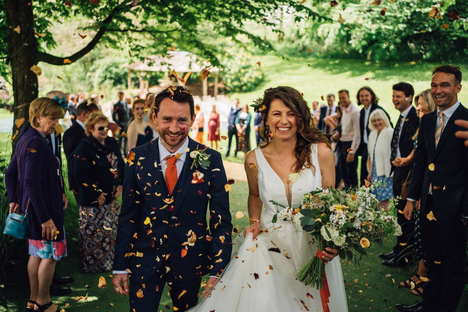 Wedding party celebrates with confetti toss in lush garden setting.