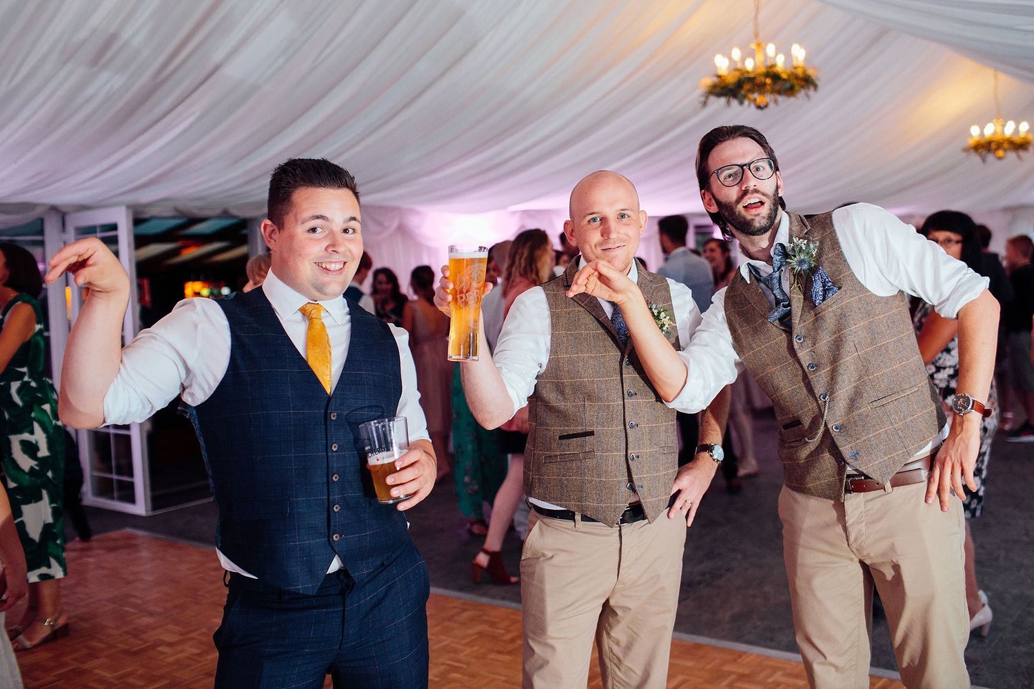 Three guests in vests dance together during a lively wedding reception celebration.