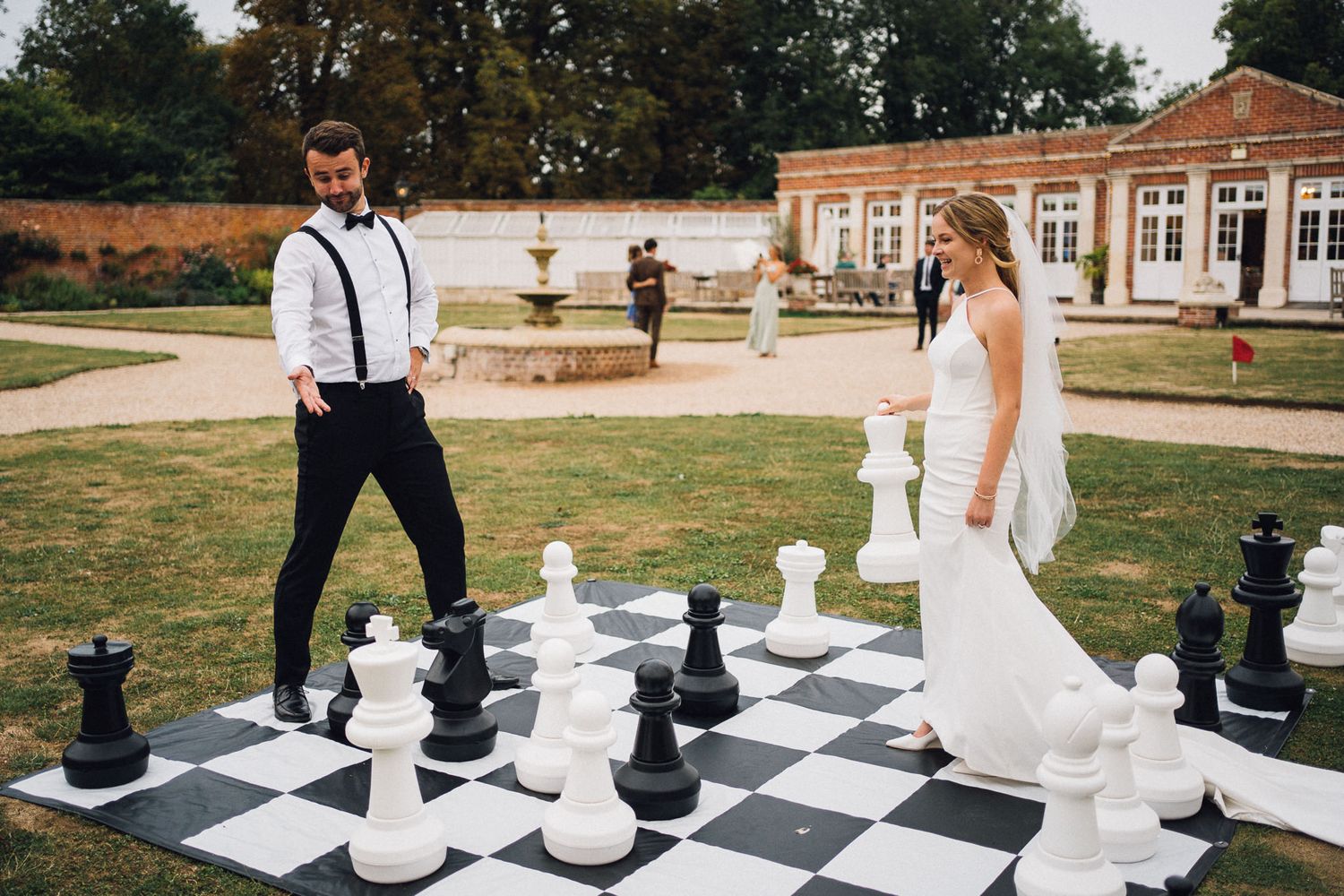A couple plays a game of life-sized chess outdoors during their wedding.