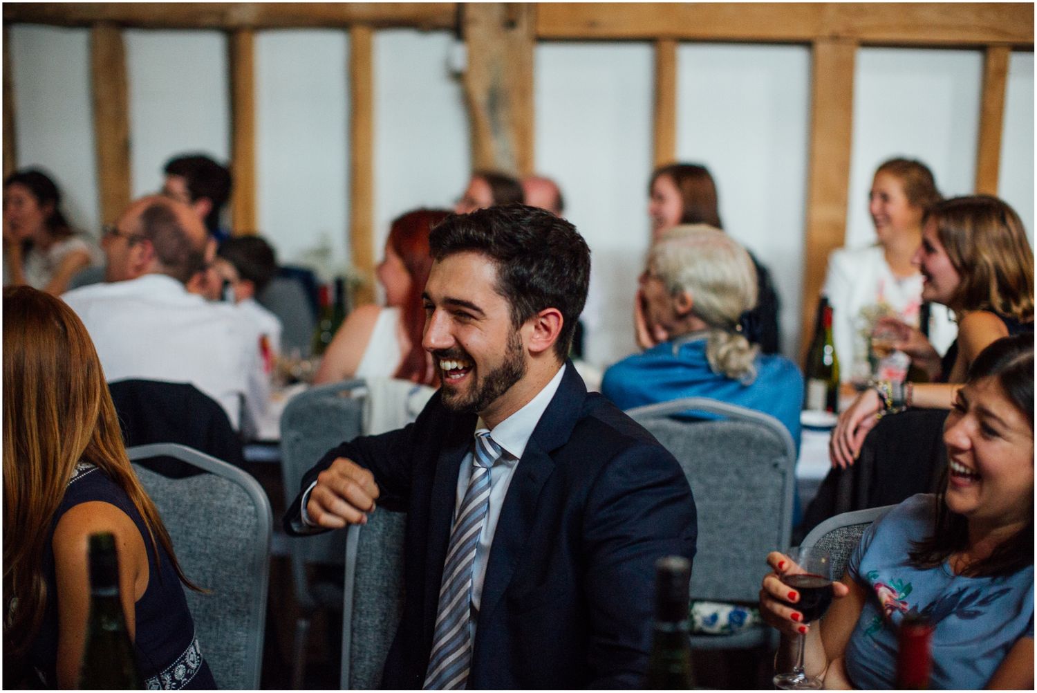Wedding reception guests enjoying dinner and conversation at rustic indoor venue.