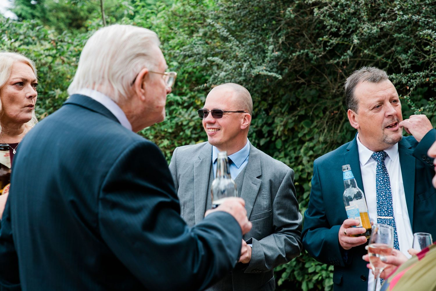 Wedding guests mingle and socialize outdoors in formal attire during a garden reception.