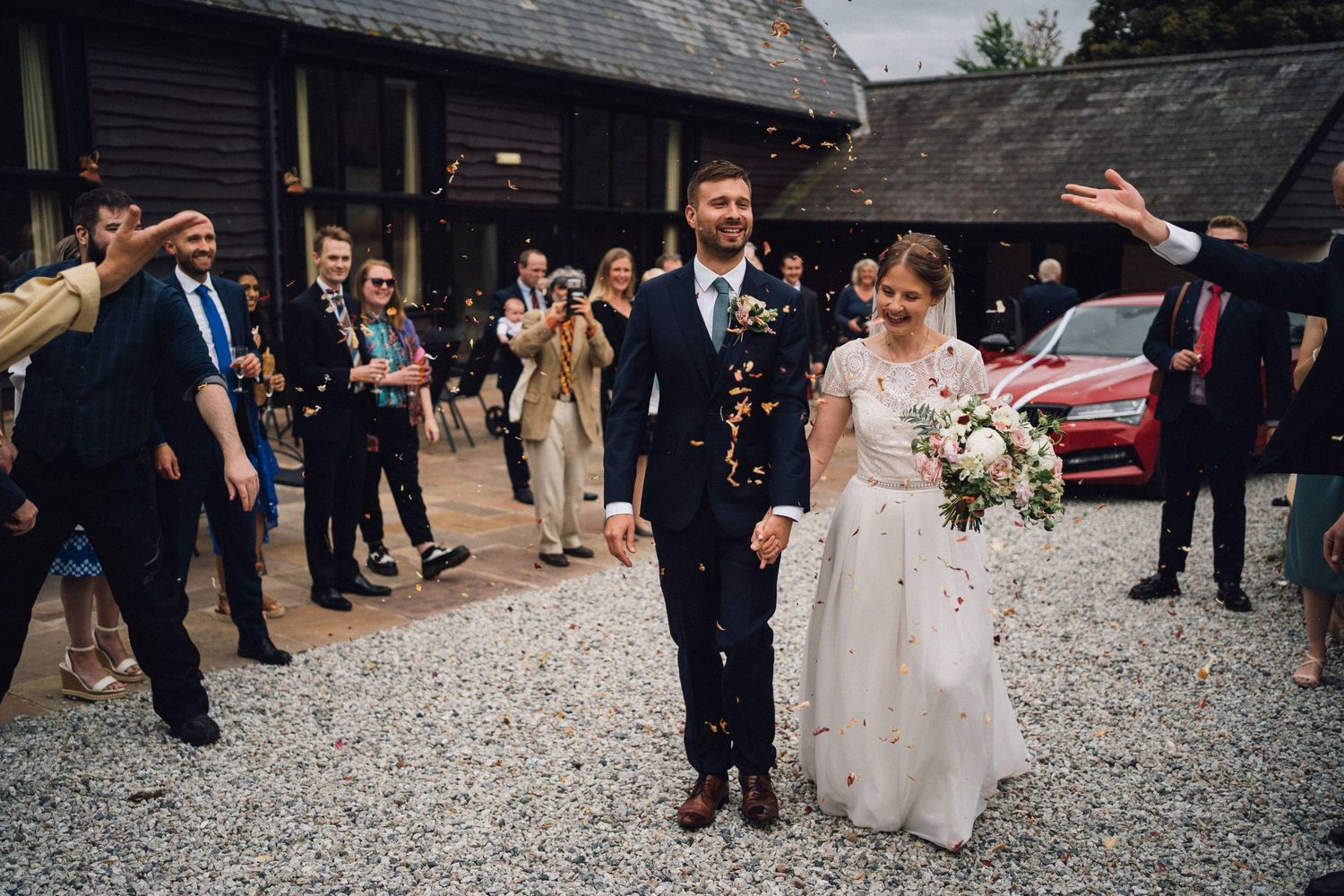 Wedding guests gather on a gravel courtyard during an outdoor celebration.