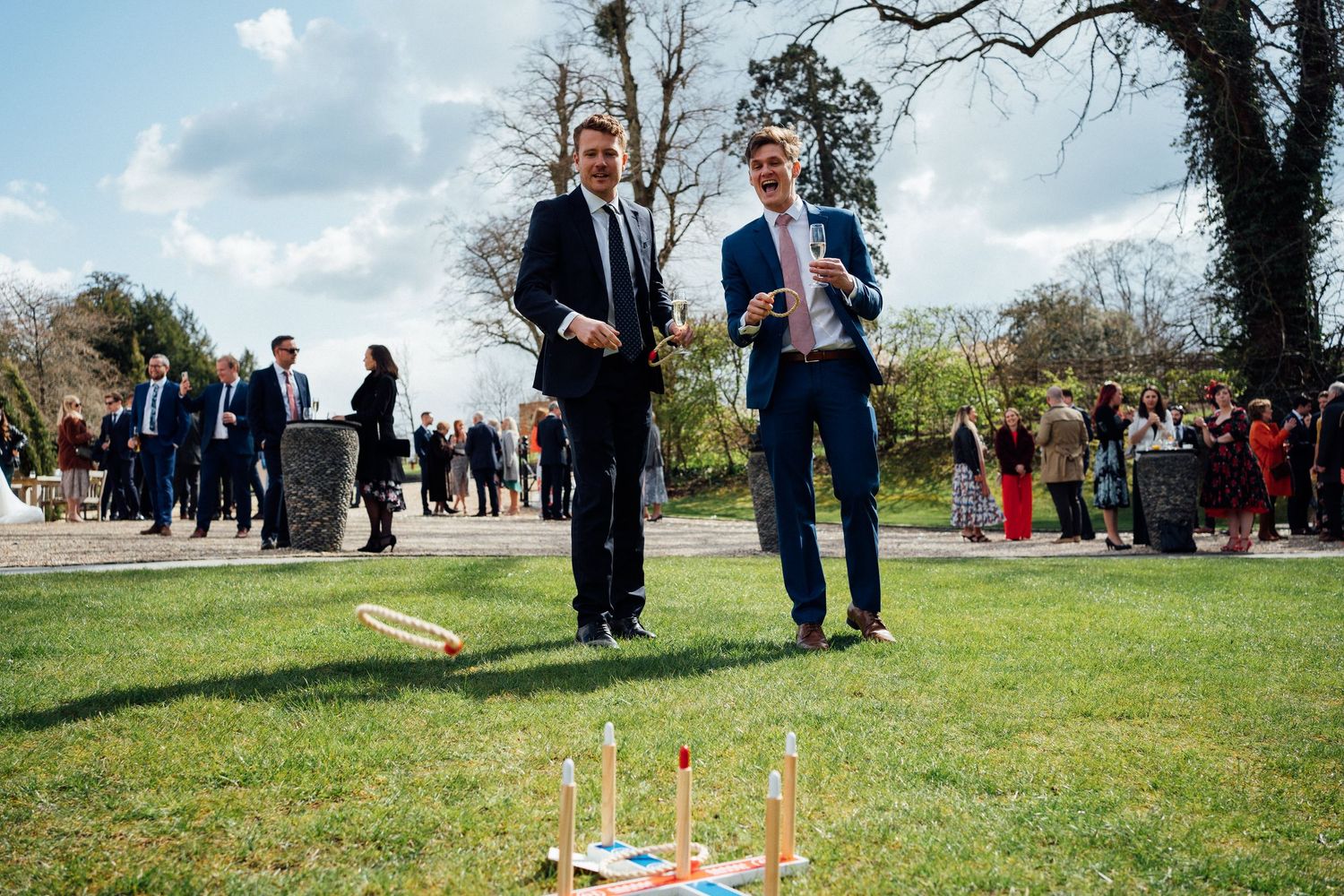 People play a lawn game with wooden stakes and ropes on a sunny spring day in a grassy field.