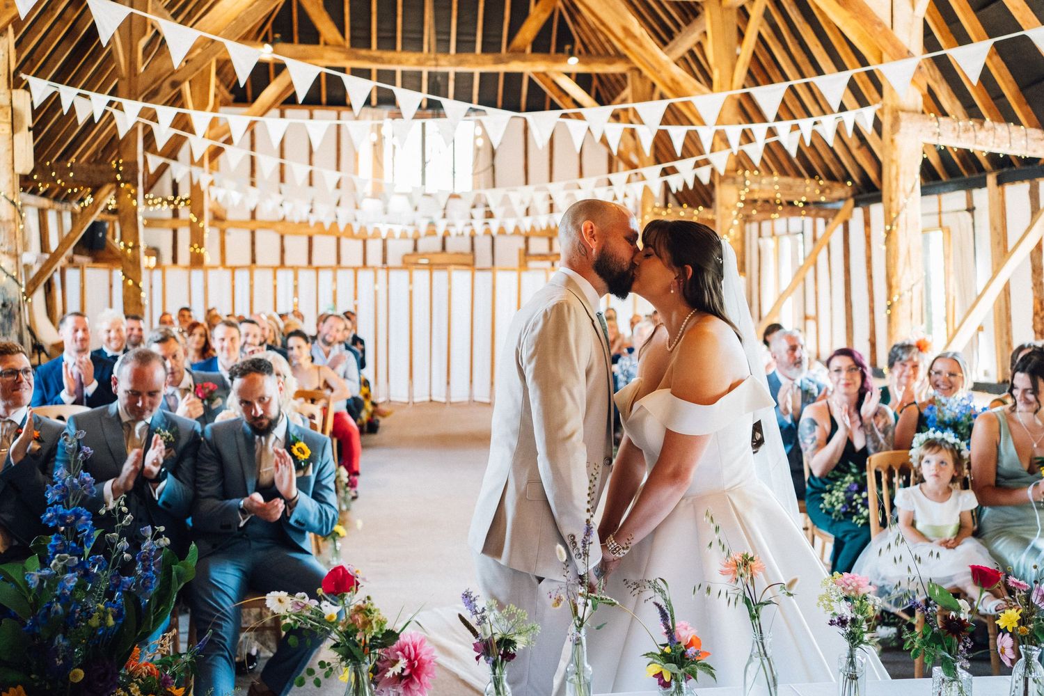 A couple shares their first dance in a rustic wooden barn decorated with string lights and floral arrangements.