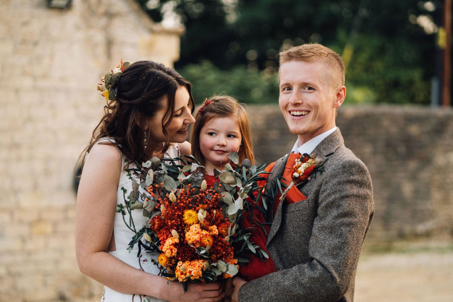 Wedding party poses together outdoors with autumn-themed burgundy and orange floral bouquets.