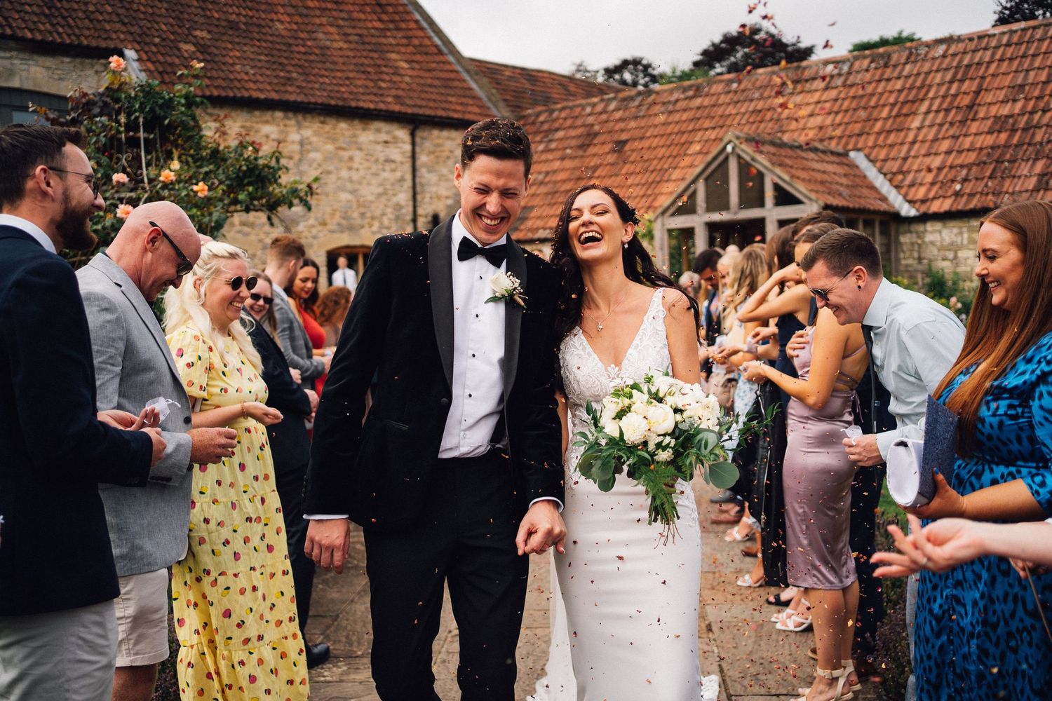 Wedding guests celebrate by throwing confetti and rice at a rustic barn venue during a joyous outdoor celebration.