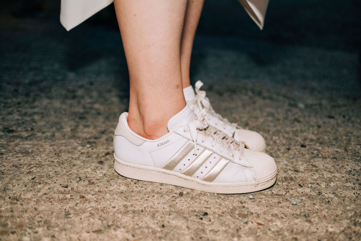 Classic white Adidas Superstar sneakers with iconic stripes worn at a wedding celebration.