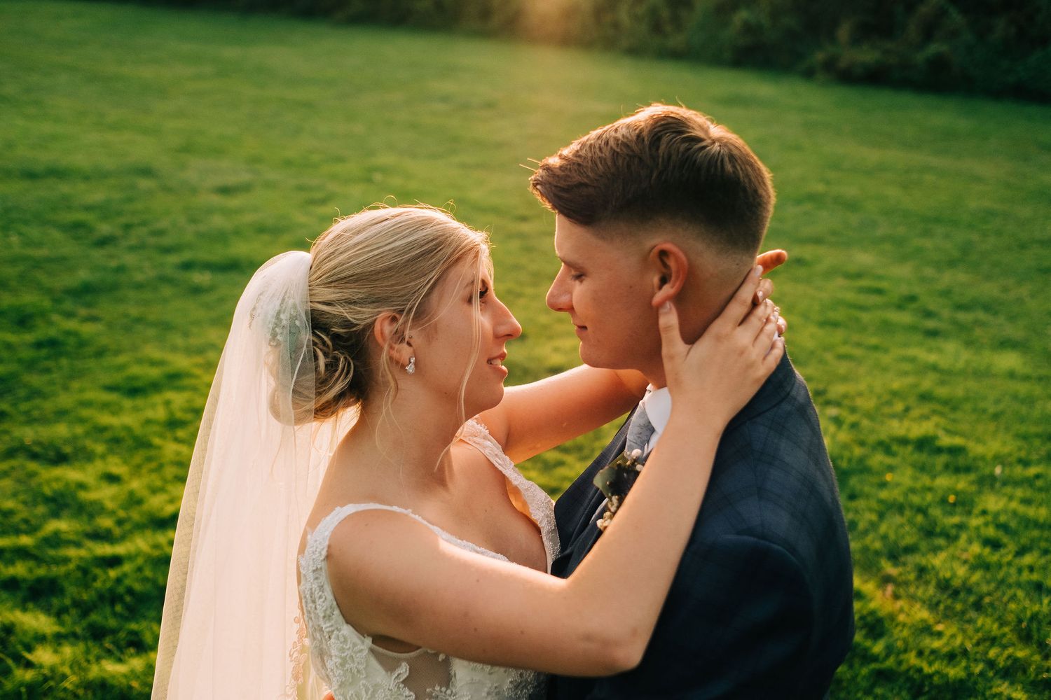 Intimate wedding portrait in golden evening light on grassy hillside.