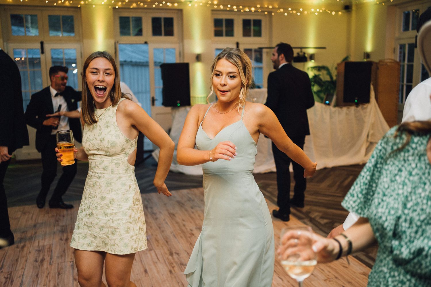 Wedding party dancing and celebrating on a wooden dance floor decorated with string lights.