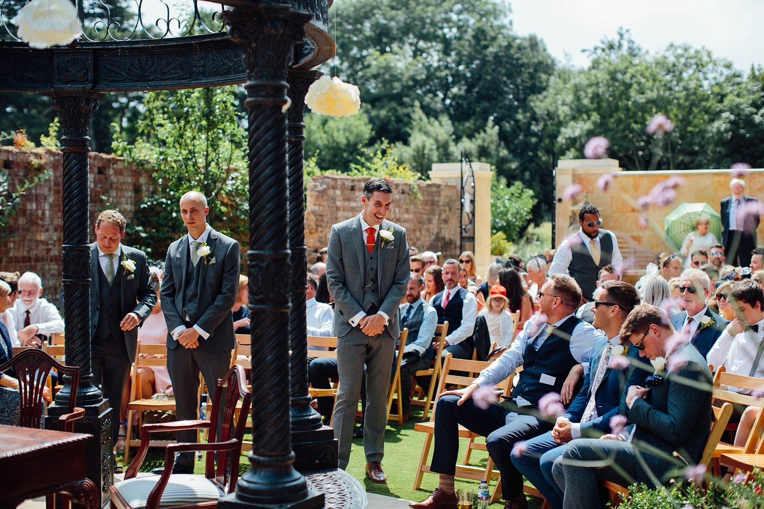 Wedding guests seated in wooden chairs at an outdoor garden ceremony.