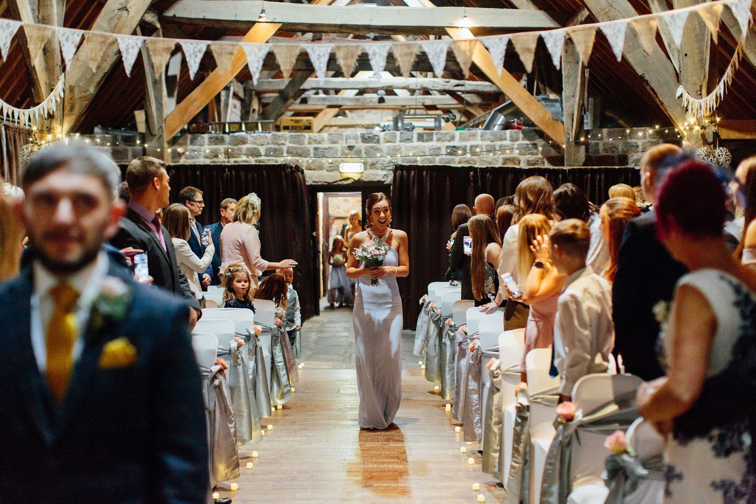 Wedding ceremony setup in a rustic barn with white bunting decorations and wooden chairs.