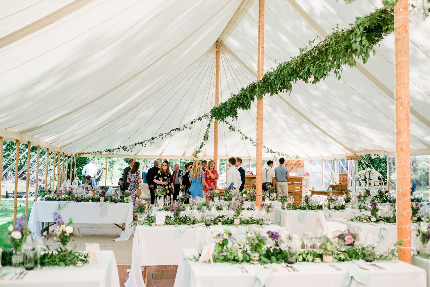 Elegant white wedding tent decorated with greenery garlands and string lights for an outdoor reception.