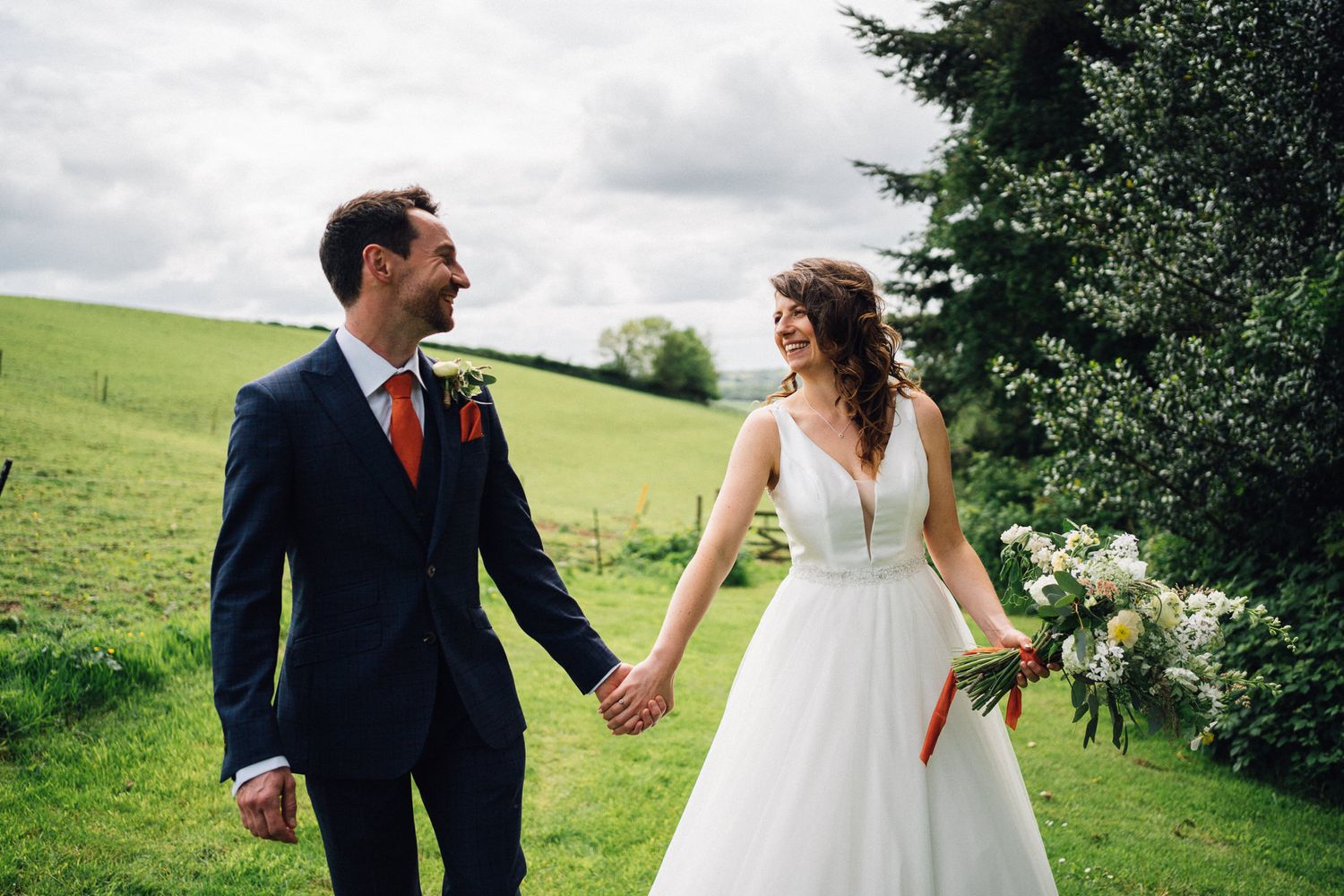 Newlyweds walk hand in hand through a lush green garden setting during their wedding celebration.