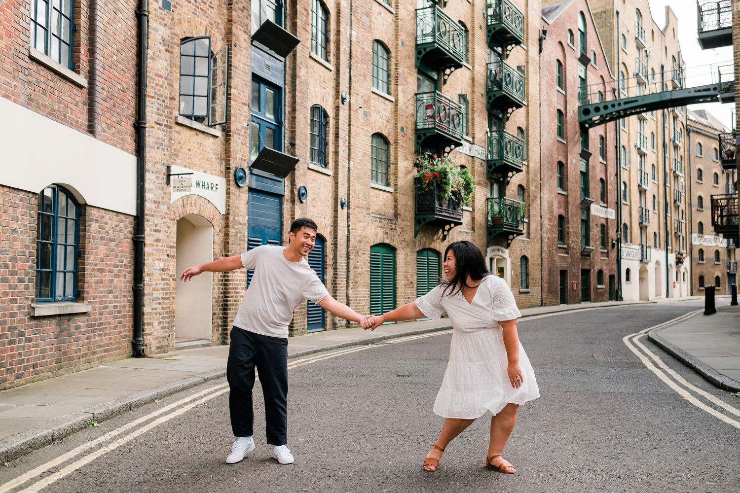 Couple dancing and twirling on urban street surrounded by historic brick buildings.