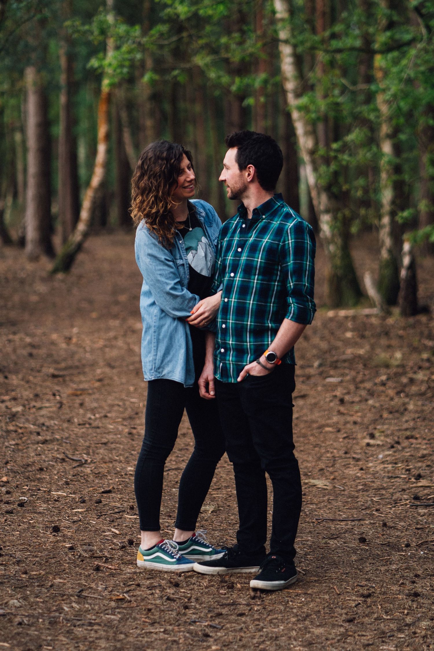 A couple shares playful moments on a forest path surrounded by tall trees.