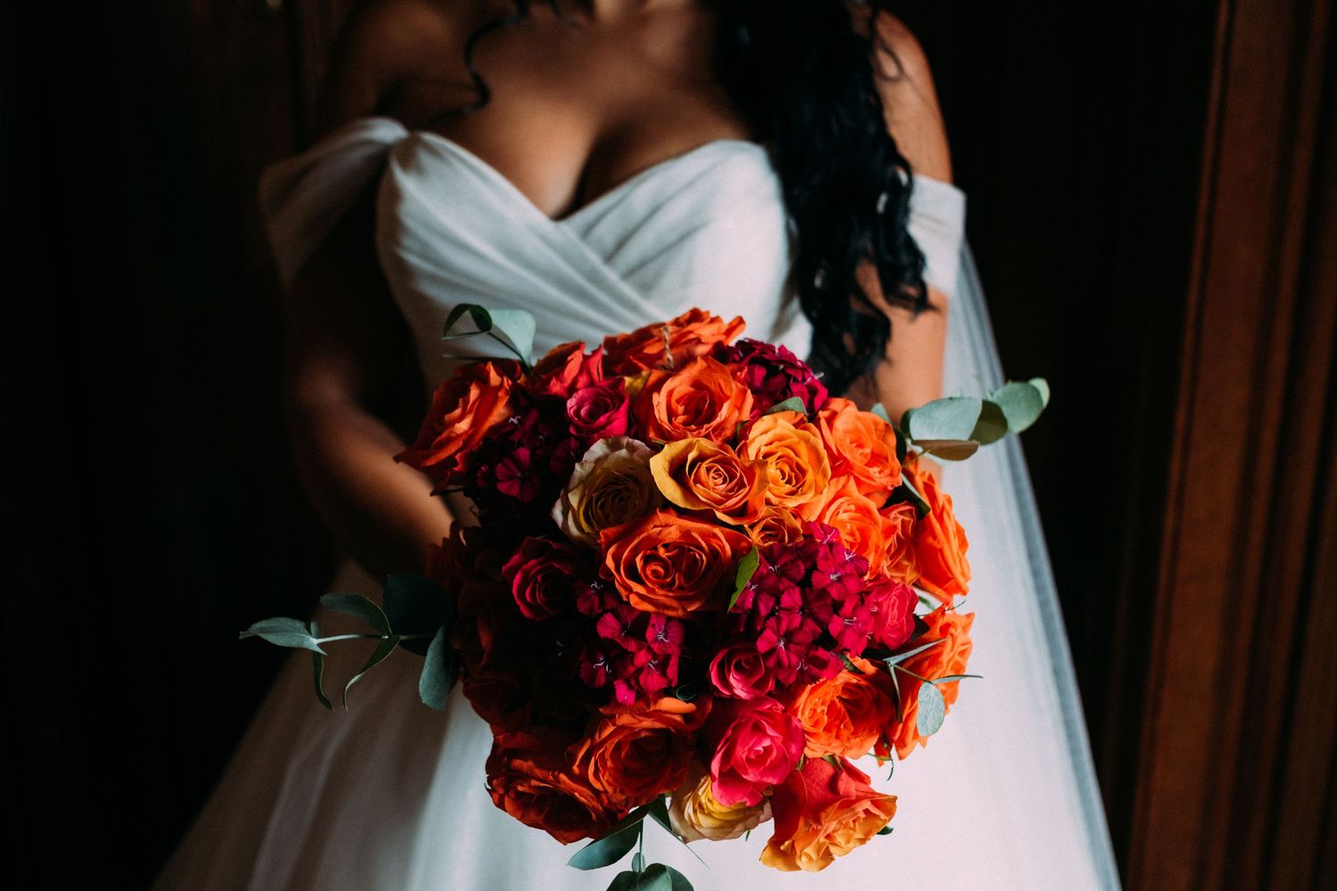 Vibrant orange and red rose wedding bouquet against a white dress.
