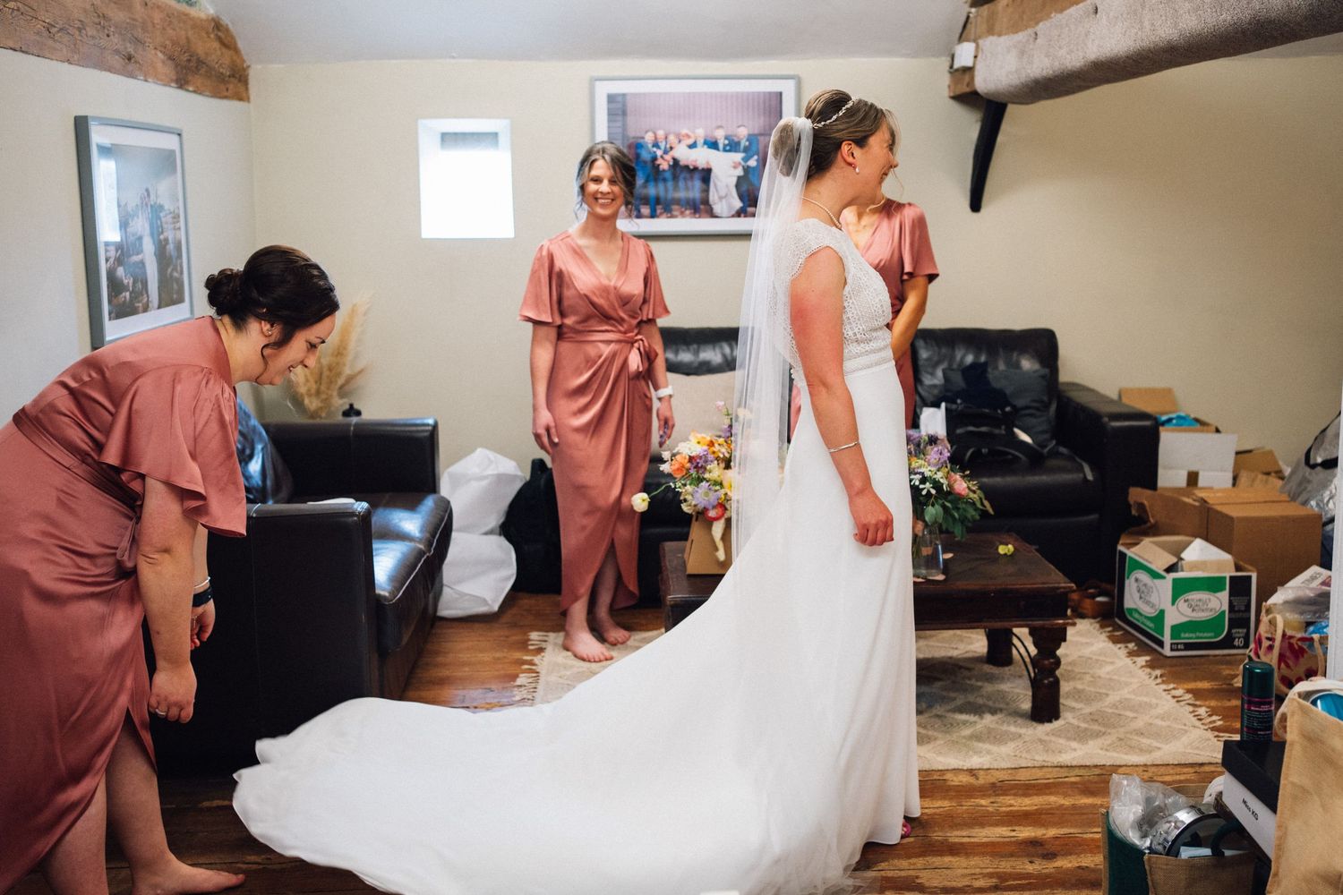 Bridesmaids help adjust the wedding dress in a bright indoor setting.