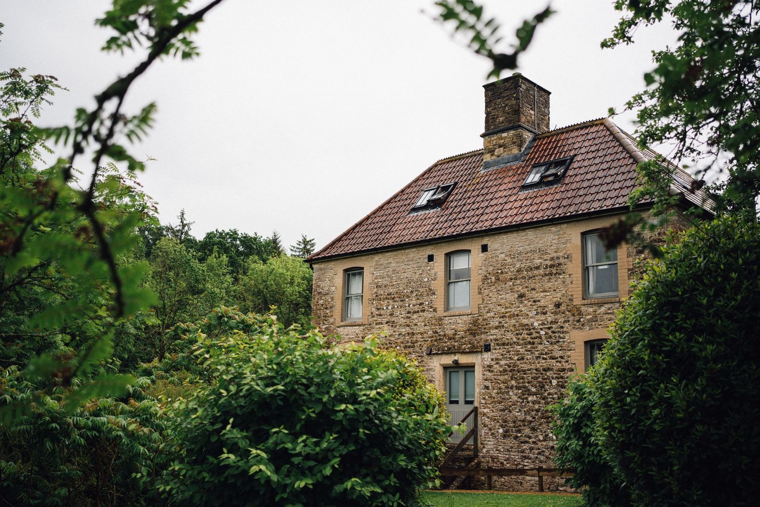 Traditional stone buildings with tiled roofs nestled among green trees on a country estate.