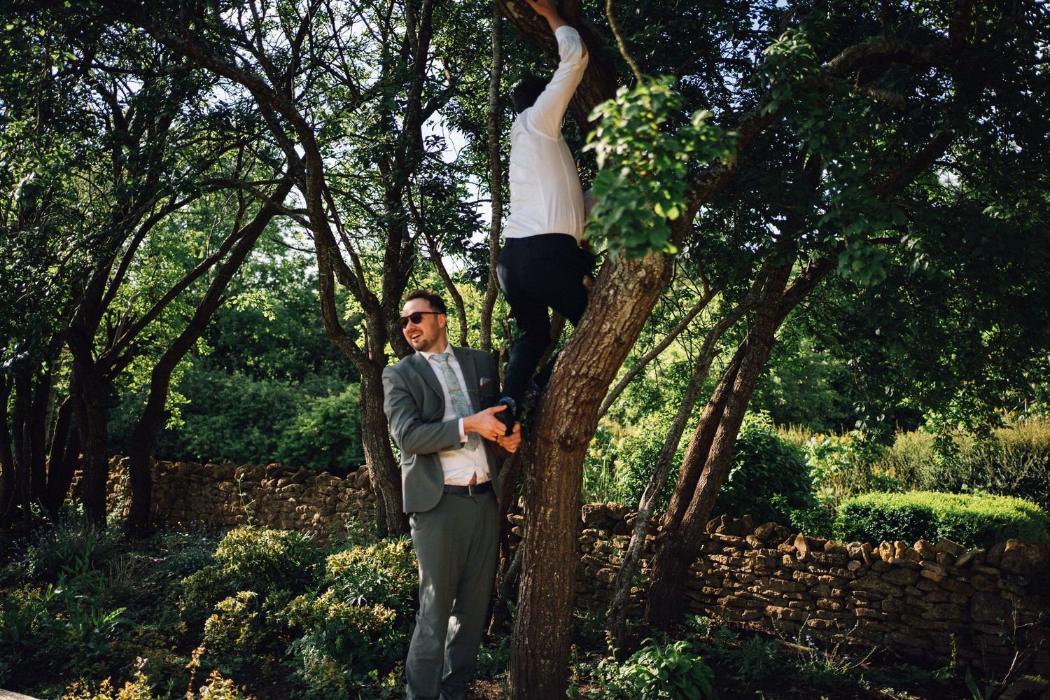 Wedding party gathered under green trees in natural outdoor setting.