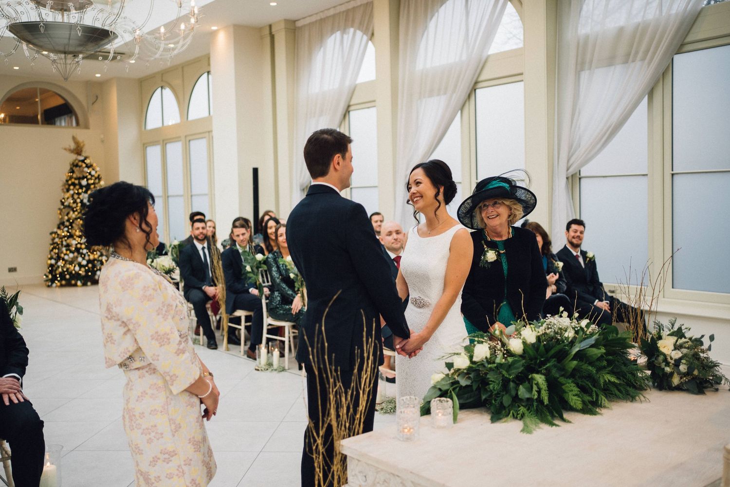 Wedding celebration in a bright conservatory space with white drapes and decorative greenery.
