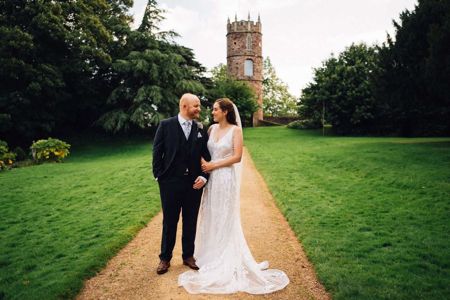 Wedding couple posing on garden grounds with historic church tower in the background.