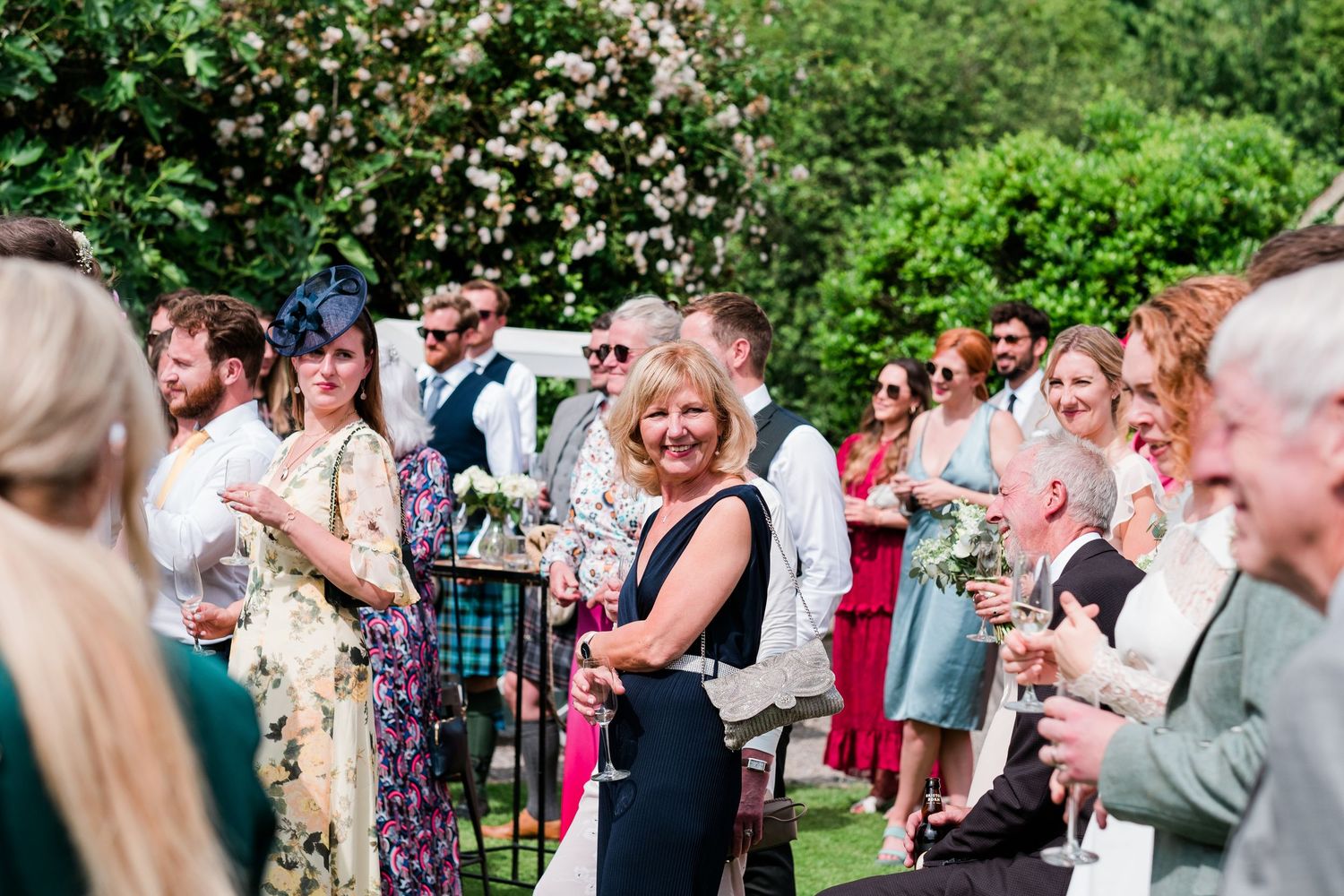 Wedding guests socialize on a lush green lawn during an outdoor summer reception.