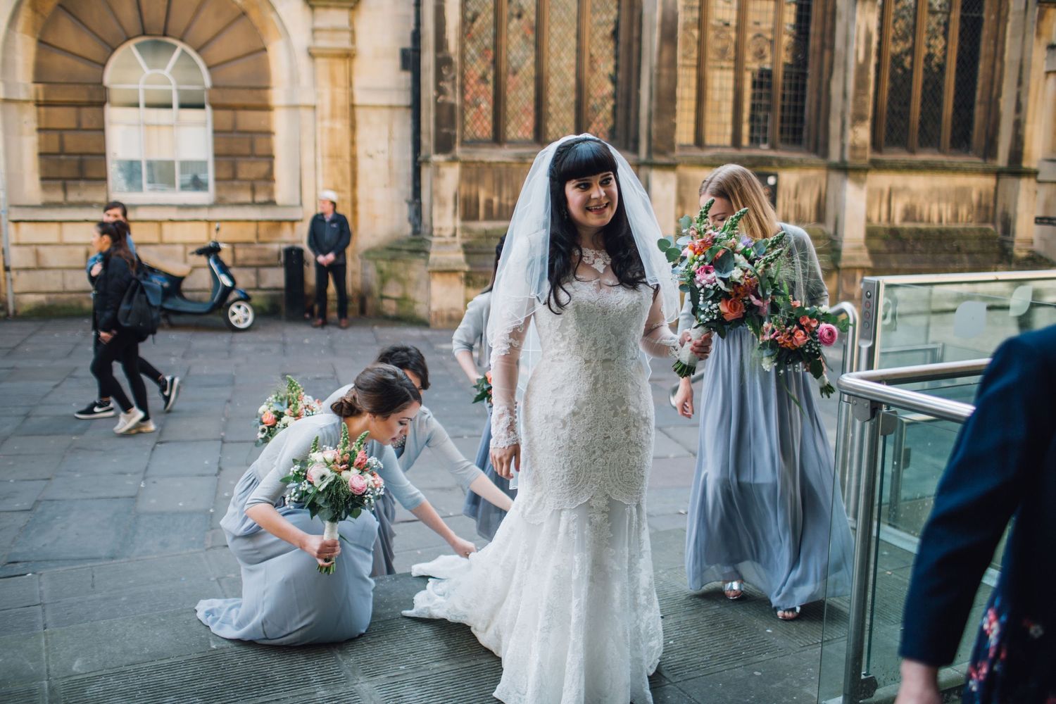 Wedding party walking through a historic stone archway with gothic architecture in the background.