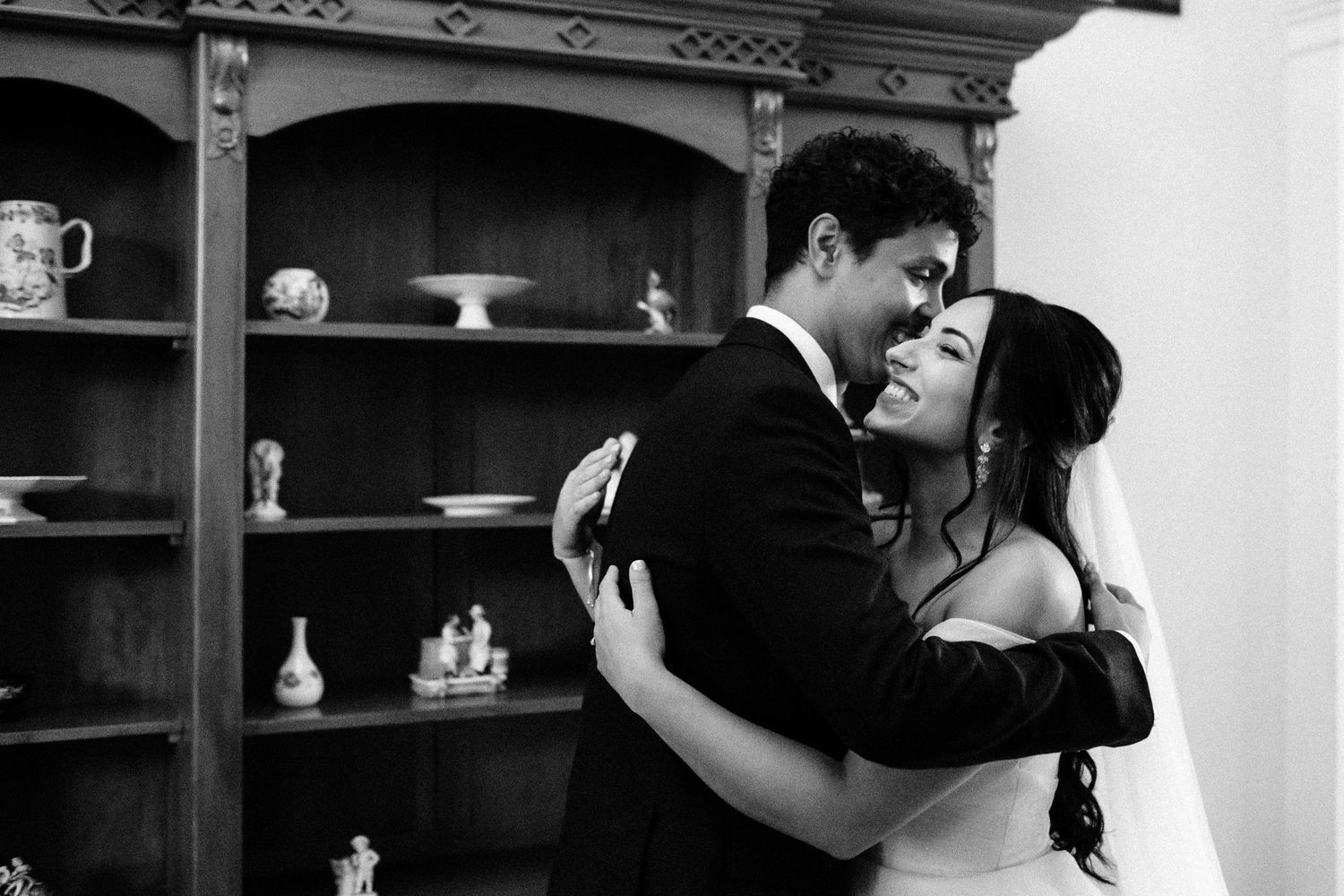 Couple embracing in front of vintage wooden shelving unit in black and white.