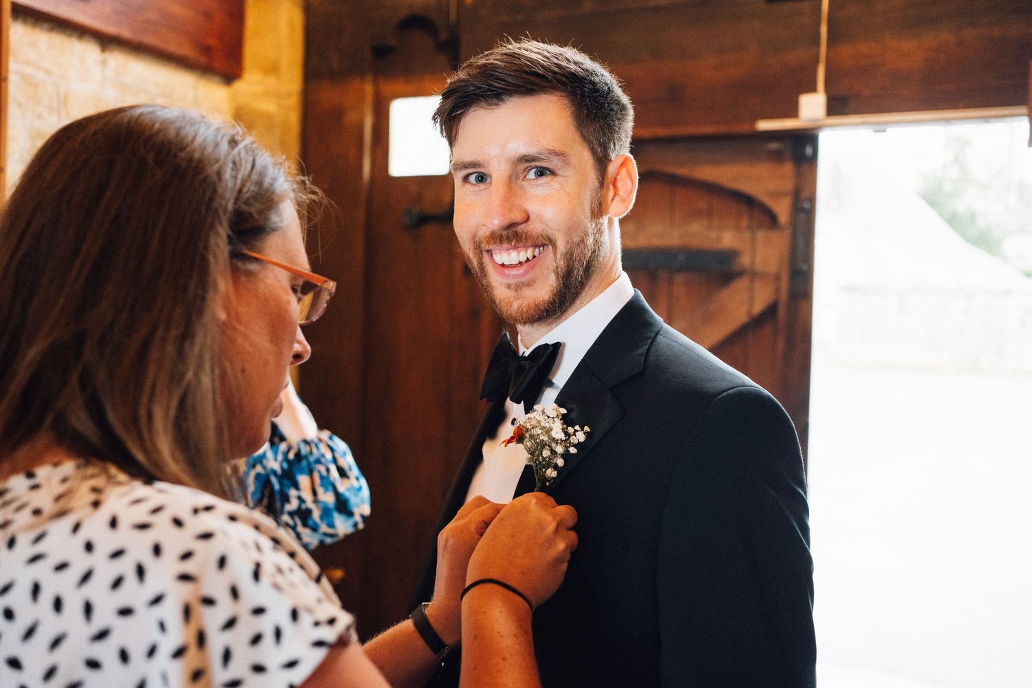 A person in formal wedding attire smiles while speaking with someone in a patterned dress.