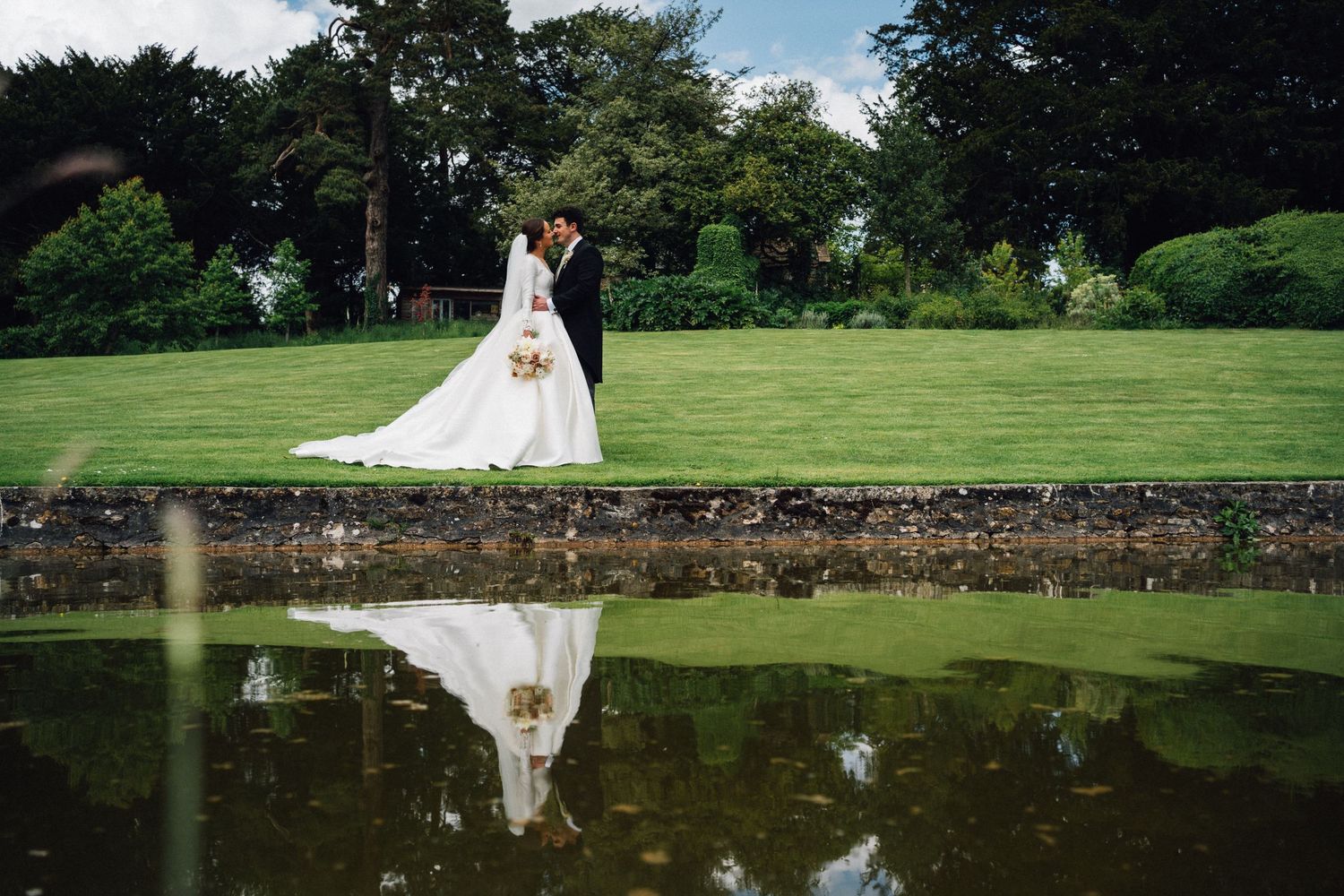 Panoramic view of wedding guests gathered on manicured grounds with reflection pond.