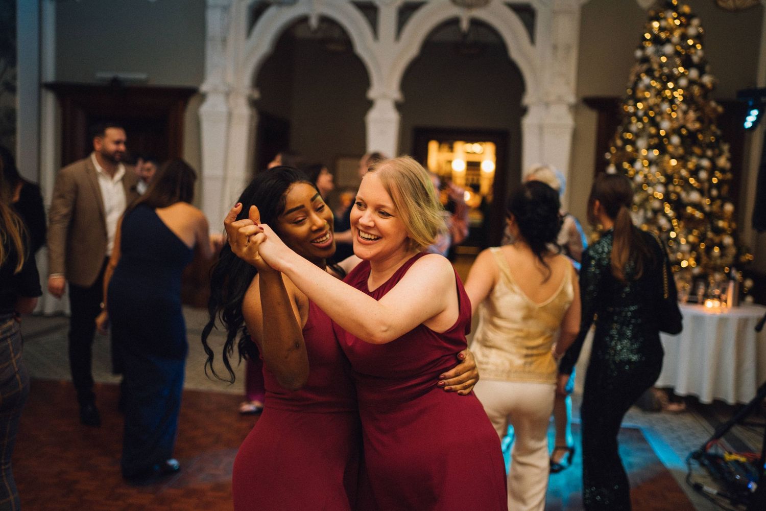 Wedding guests dancing and celebrating in an elegant venue decorated with Christmas trees and white columns.