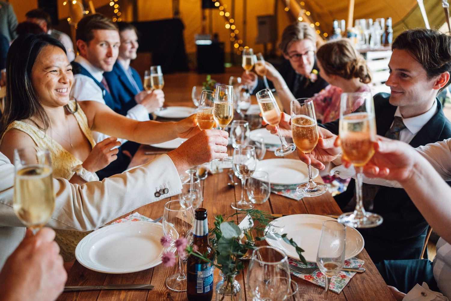 Wedding guests dining and socializing at reception tables under warm lighting.