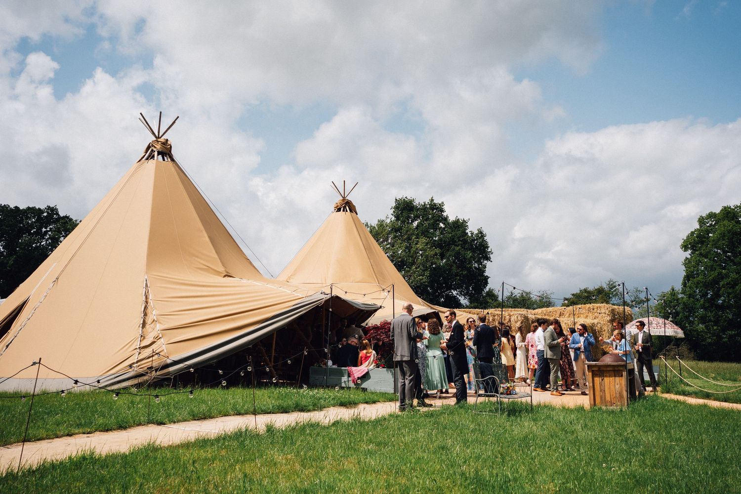 Multiple teepee-style event tents arranged on a hillside under blue skies.