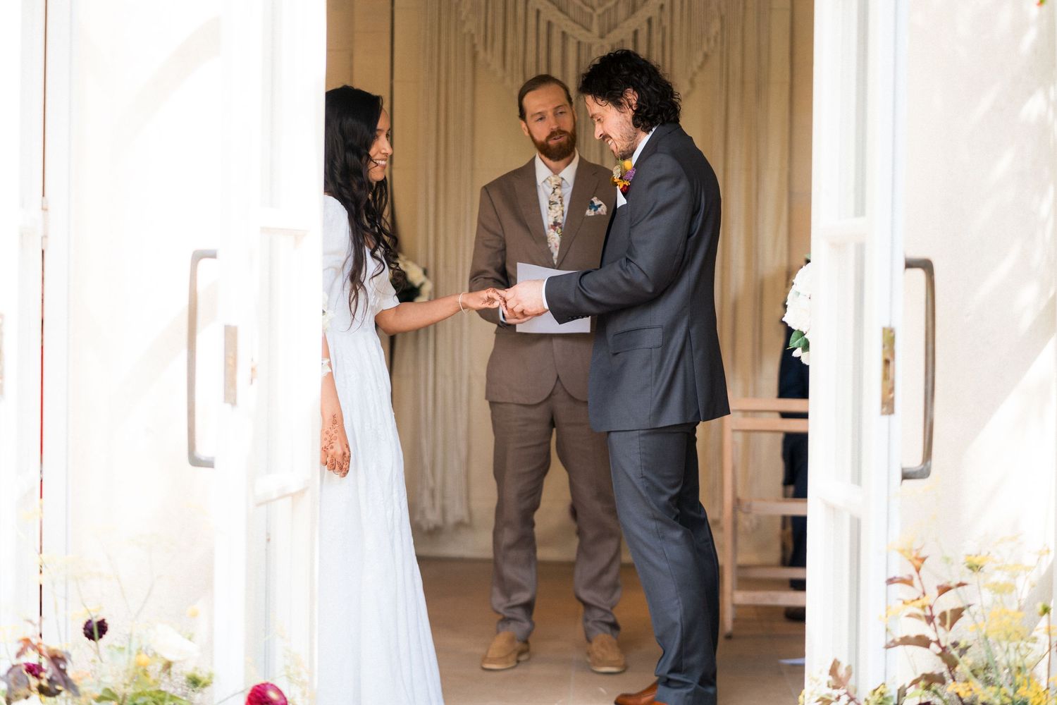 Bride and groom exchange rings during an intimate outdoor wedding ceremony with an officiant.