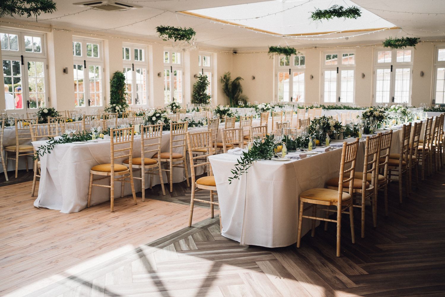 Elegant wedding reception hall set with wooden chairs and white tablecloths.