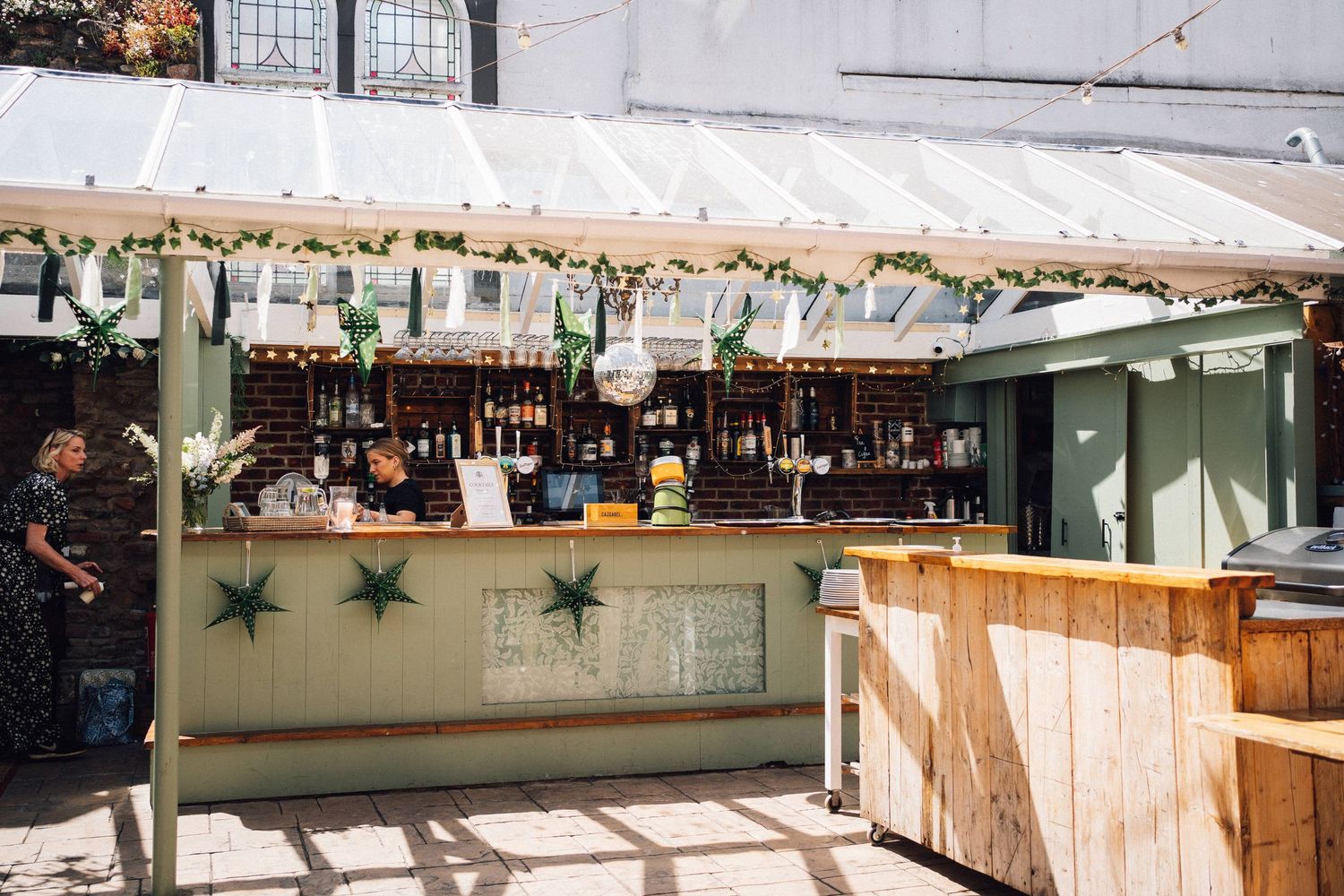 Long wooden bar counter with hanging lights and shelving displays in an indoor commercial space.